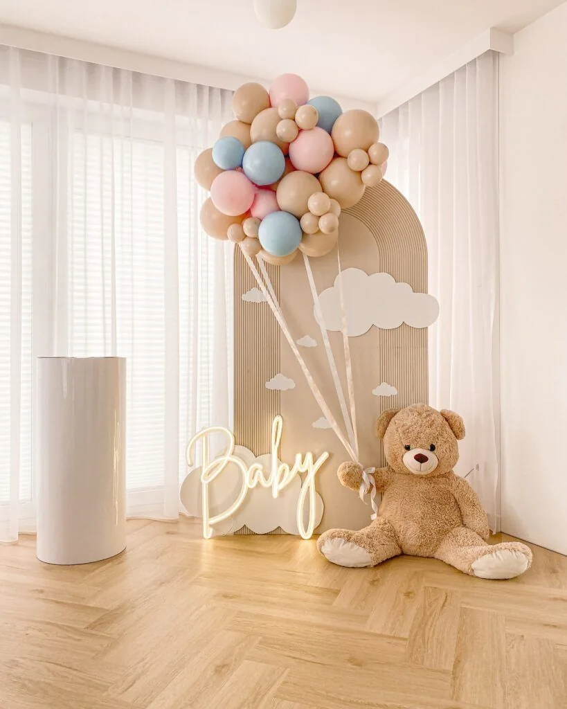 Allestimento baby shower con fondale chiaro, palloncini pastello e orsetto.