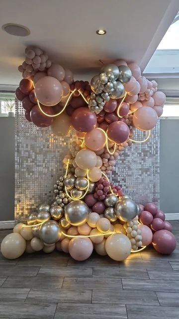 Composizione con palloncini rosa, argento e oro e dettagli luminosi.