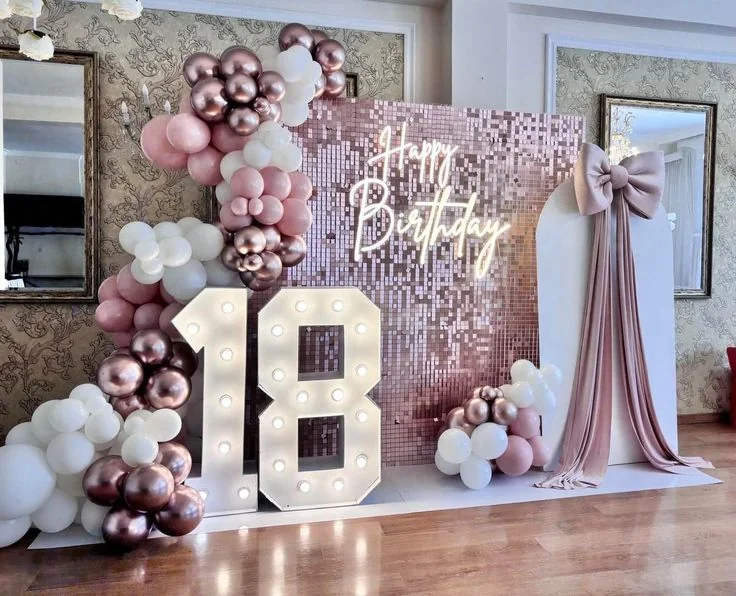 Diciottesimo con numero 18 luminoso, fondale rosa e palloncini cipria e rose gold.
