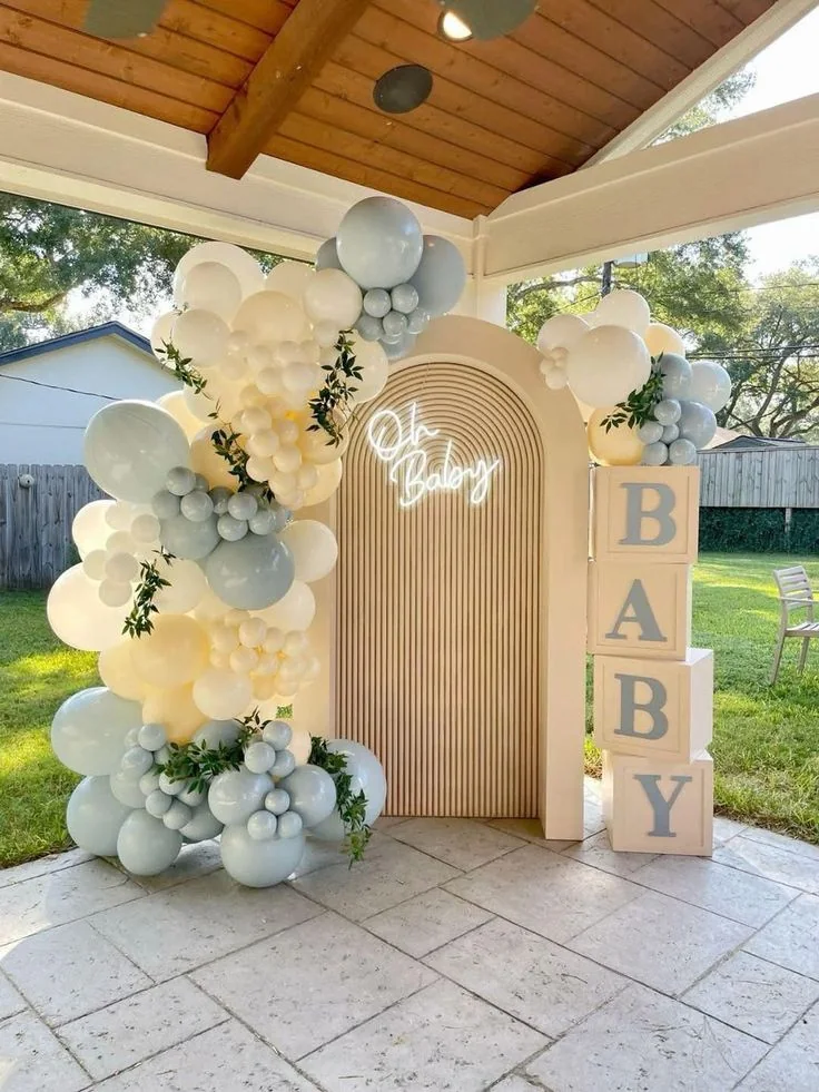 Allestimento baby shower con fondale ad arco, lettere BABY e palloncini azzurri e avorio.