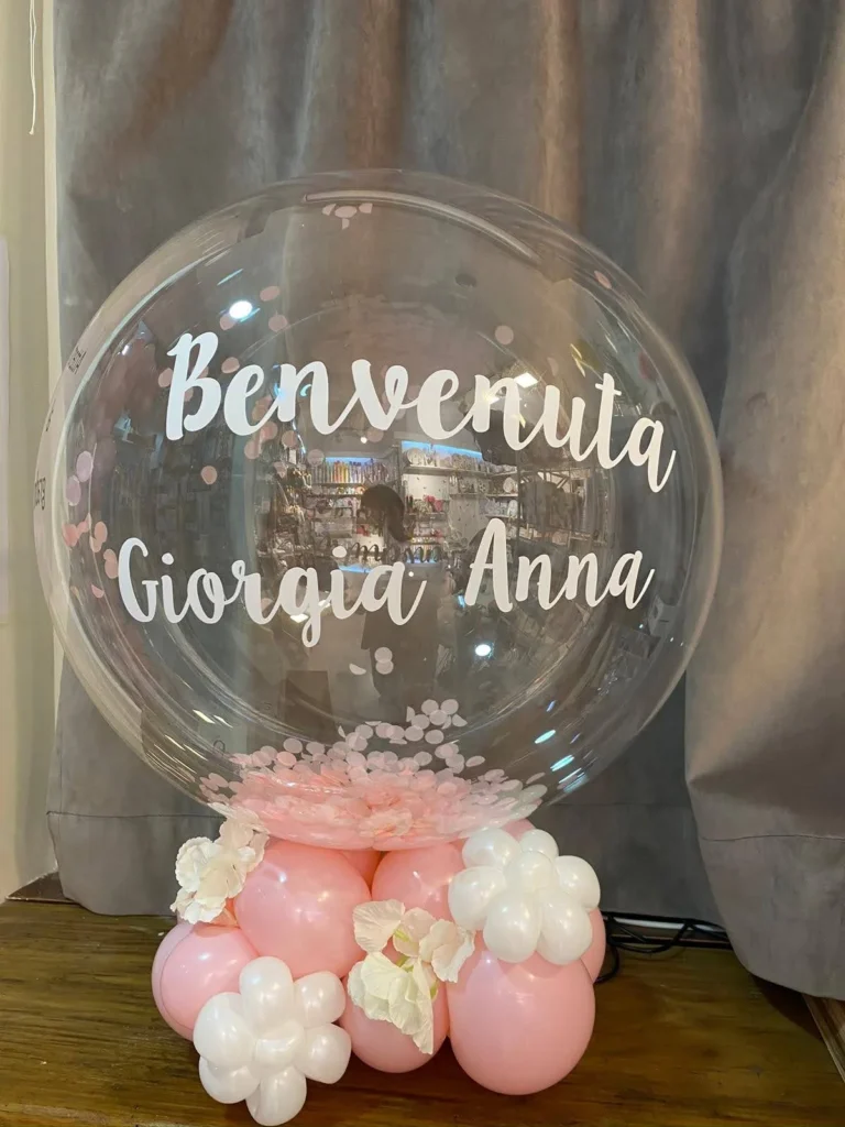 Bolla trasparente personalizzata per una nascita, con base di palloncini rosa e bianchi.
