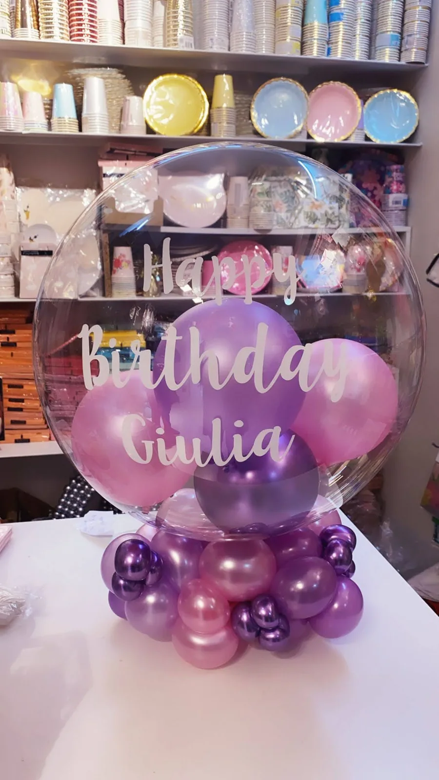 Bolla trasparente personalizzata per compleanno con palloncini viola e rosa.