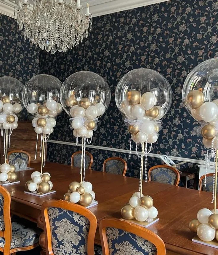Centrotavola con bolle trasparenti, piccoli palloncini bianchi e oro e basi coordinate.