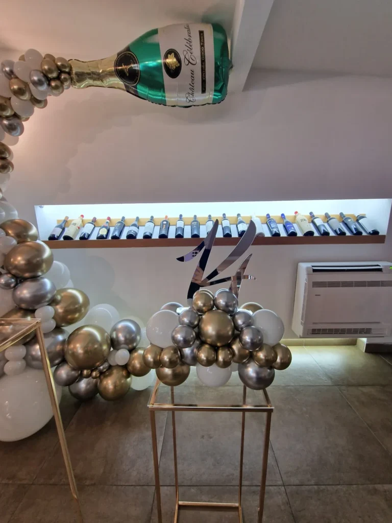 Composizione decorativa con bottiglia e palloncini argento, bianchi e trasparenti.